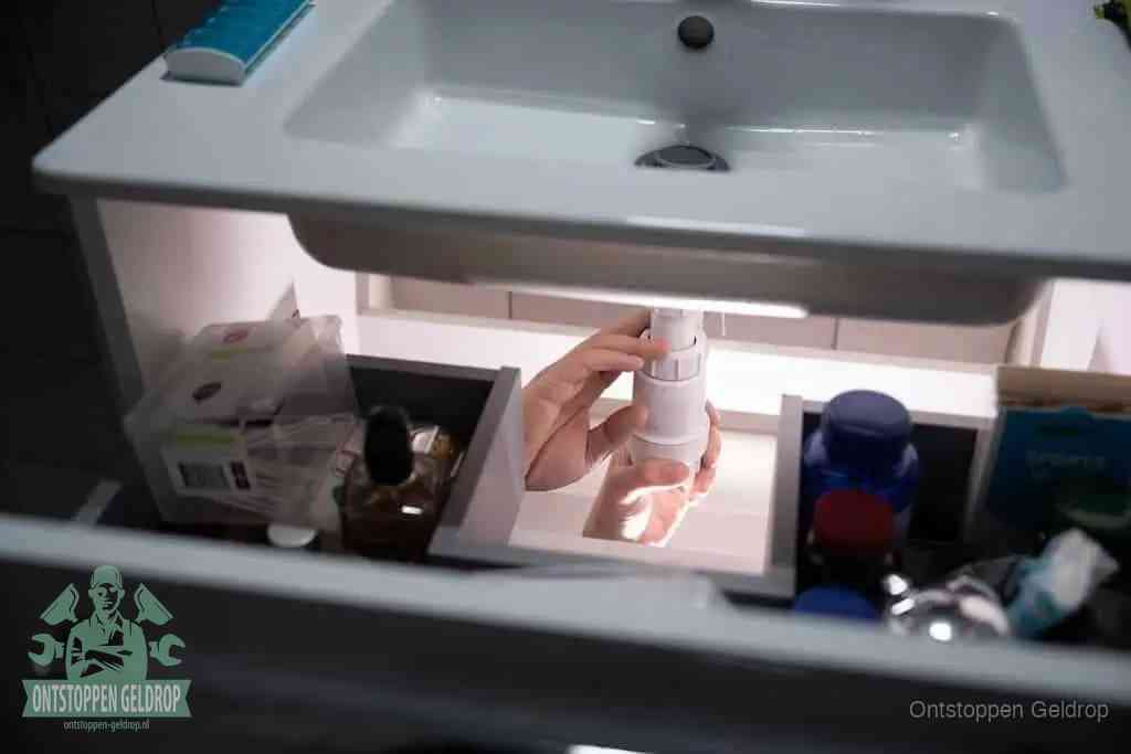 Een pompfles met zeep boven een wastafel, de heet water en afwasmiddel-methode om een vetprop in de afvoer los te maken in Geldrop