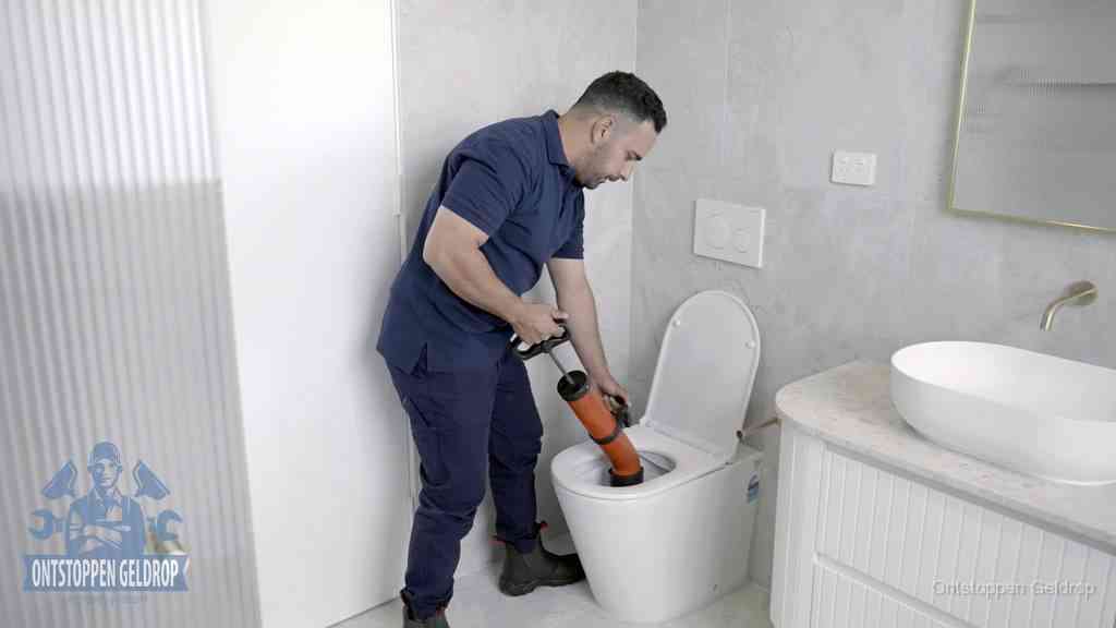 Een monteur buigt over een wandcloset en duwt met de hand een persluchtontstopper in de toiletpot om de verstopping handmatig los te maken in Geldrop Een monteur buigt over een wandcloset en duwt met de hand een persluchtontstopper in de toiletpot om de verstopping handmatig los te maken in Geldrop