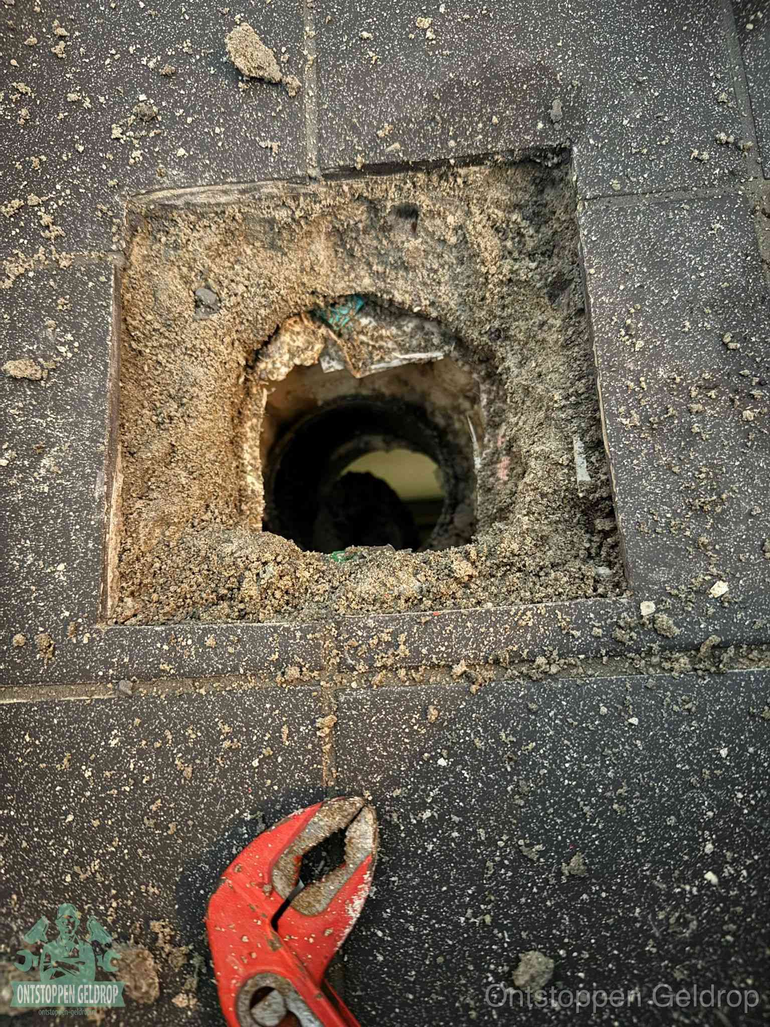 Een geopend rioolputje in een betontegelvloer met losgemaakt rooster en een zichtbare ronde afvoerbuis, het achterhalen waar de afvoerverstopping zit in Geldrop