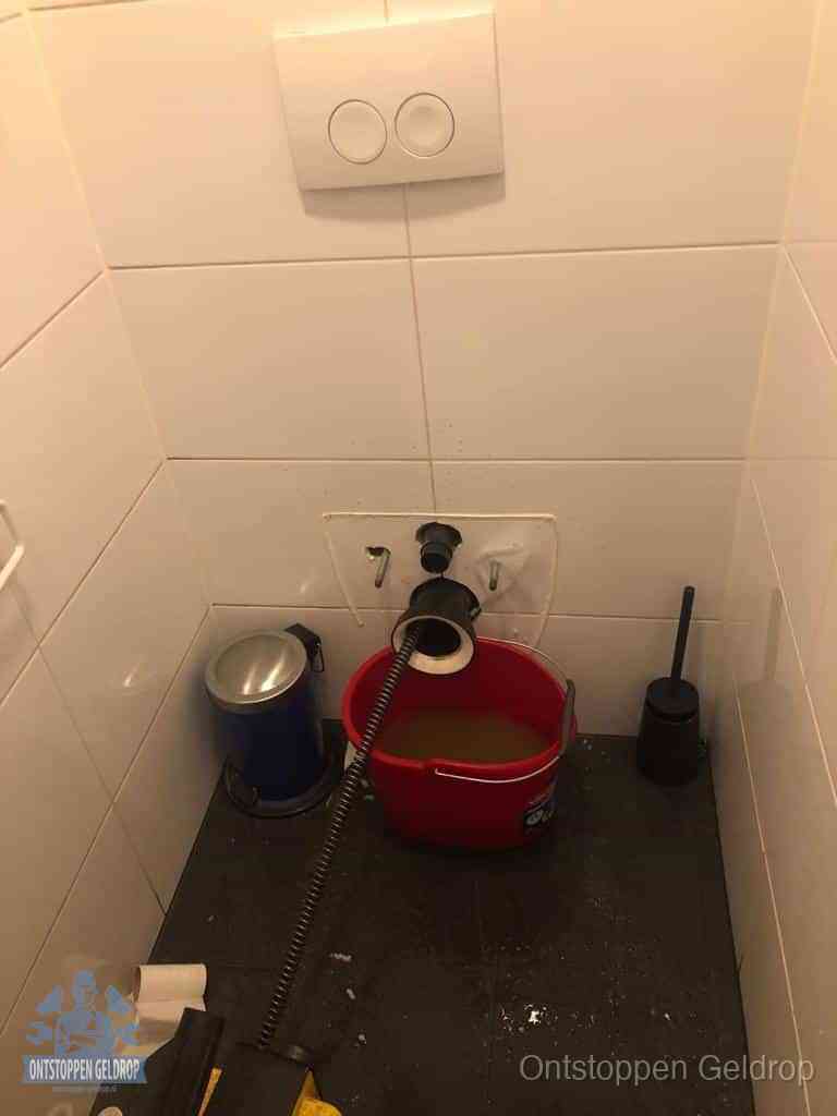 Een ontstopte wand-wc met verwijderde toiletpot waar een ontstoppingsveer in de wanduitgang verdwijnt, het achterhalen waar de verstopping zit in Geldrop Een ontstopte wand-wc met verwijderde toiletpot waar een ontstoppingsveer in de wanduitgang verdwijnt, het achterhalen waar de verstopping zit in Geldrop