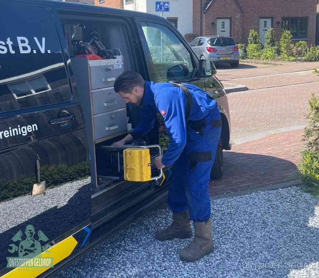 Een monteur pakt buiten op de oprit gereedschap uit de bedrijfsbus, het moment om een professional in te schakelen voor een verstopte afvoer in Geldrop