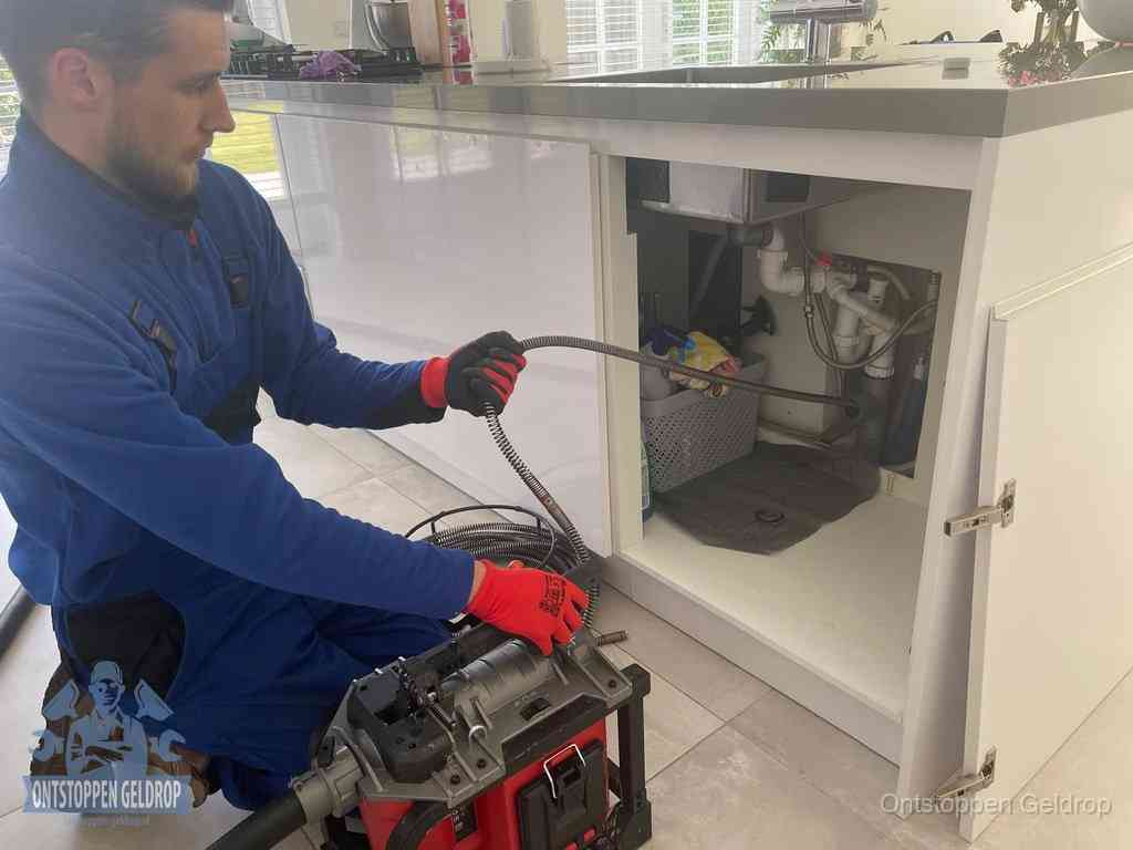 Monteur voert een ontstoppingsveer in de afvoer onder de keuken in Geldrop