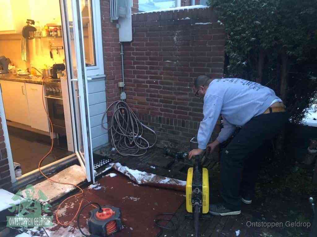 Een monteur werkt buiten bij een open riool-/grondput met een elektrische ontstoppingsmachine om een verborgen afvoerprobleem op te sporen in Geldrop