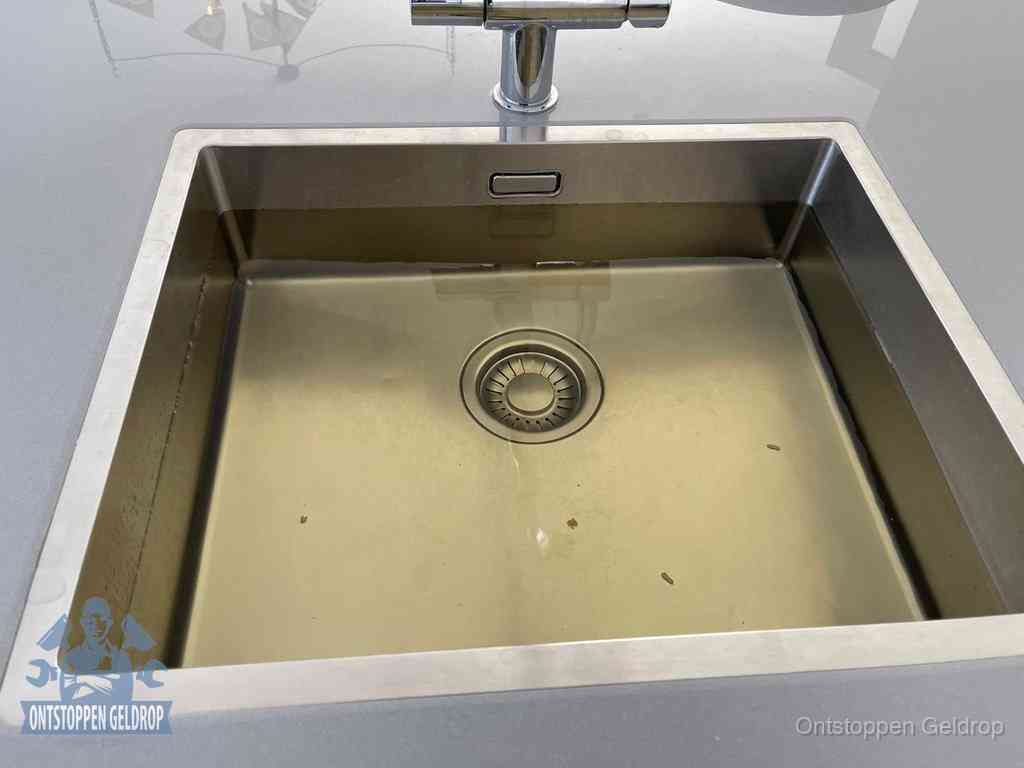Stilstaand water in een rvs spoelbak dat niet wegloopt, een duidelijk signaal van een gootsteenverstopping in Geldrop