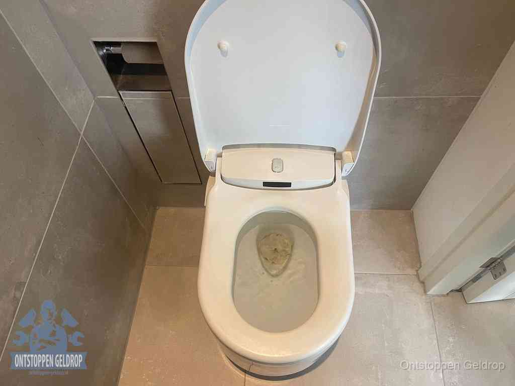 Een wit hangtoilet waarin een prop wc-papier op het water blijft drijven, een duidelijk signaal van een verstopte wc in Geldrop
