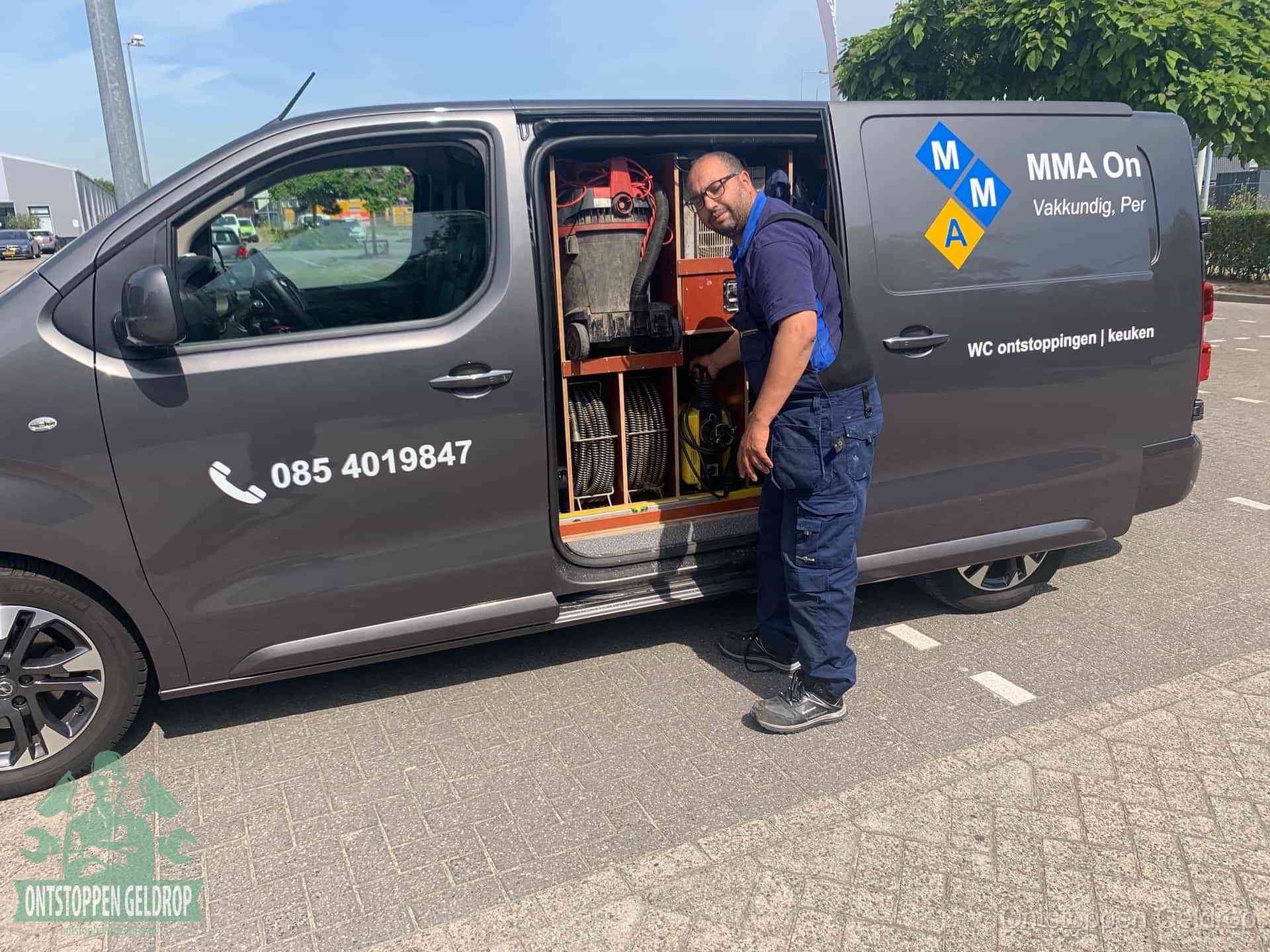 Een monteur bij de open schuifdeur van zijn bedrijfsbus op een parkeerplaats, klaar om de oorzaak van terugkerende afvoerverstoppingen aan te pakken in Geldrop