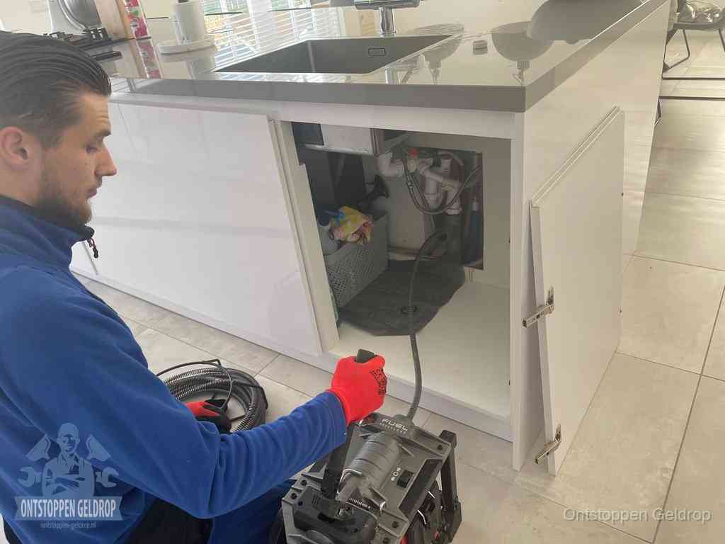 Monteur ontstopt met een veermachine een verstopte afvoer onder de gootsteen in Geldrop
