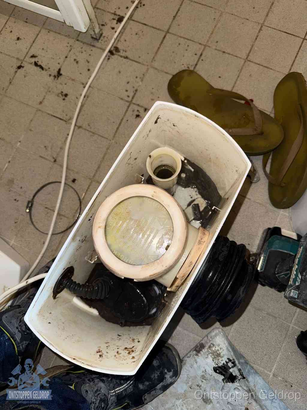 Een gedemonteerde toiletpot op de vloer met ontstoppingsveer en gereedschap ernaast, het verwijderen van een vastzittend voorwerp uit de wc in Geldrop Een gedemonteerde toiletpot op de vloer met ontstoppingsveer en gereedschap ernaast, het verwijderen van een vastzittend voorwerp uit de wc in Geldrop