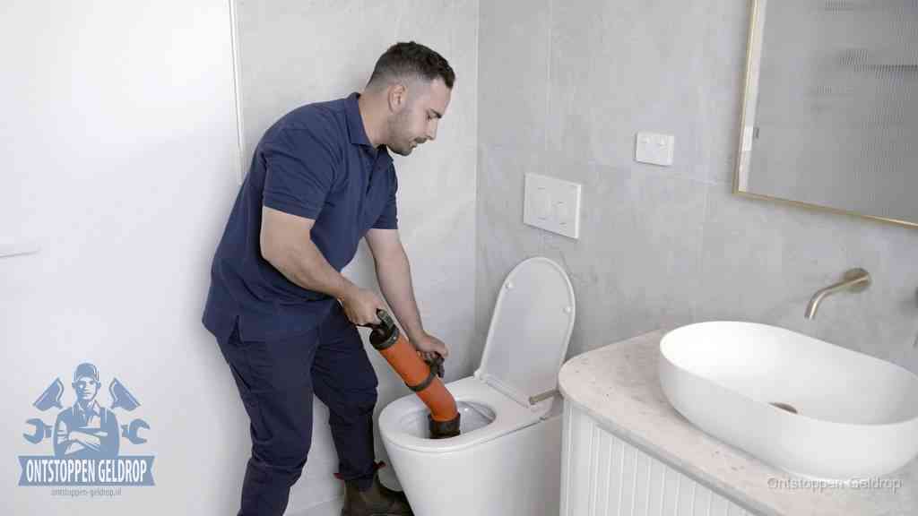 Een man gebruikt een handmatige luchtdruk-ontstopper in een modern betegeld toilet om zelf de wc te ontstoppen in Geldrop Een man gebruikt een handmatige luchtdruk-ontstopper in een modern betegeld toilet om zelf de wc te ontstoppen in Geldrop